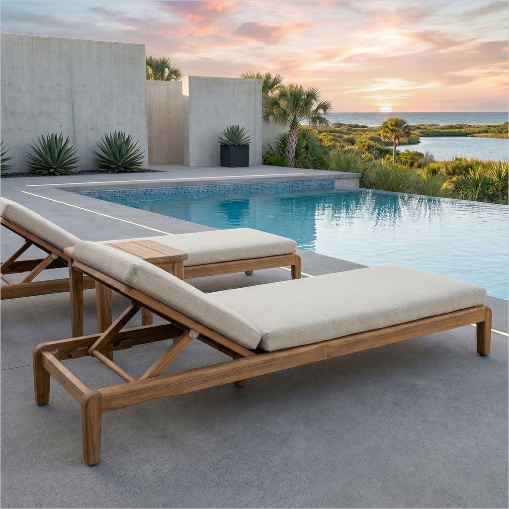 Wooden lounge chairs with beige cushions by a poolside at sunset.