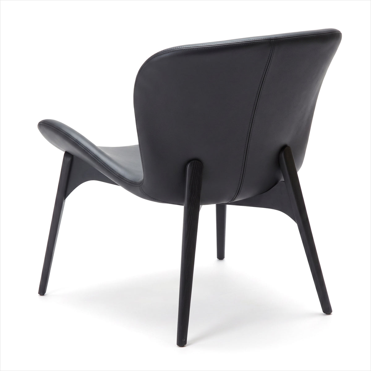 A modern black leather armchair with a sculpted curved backrest and tapered black wooden legs, shown from a three-quarters angle on a white studio background.